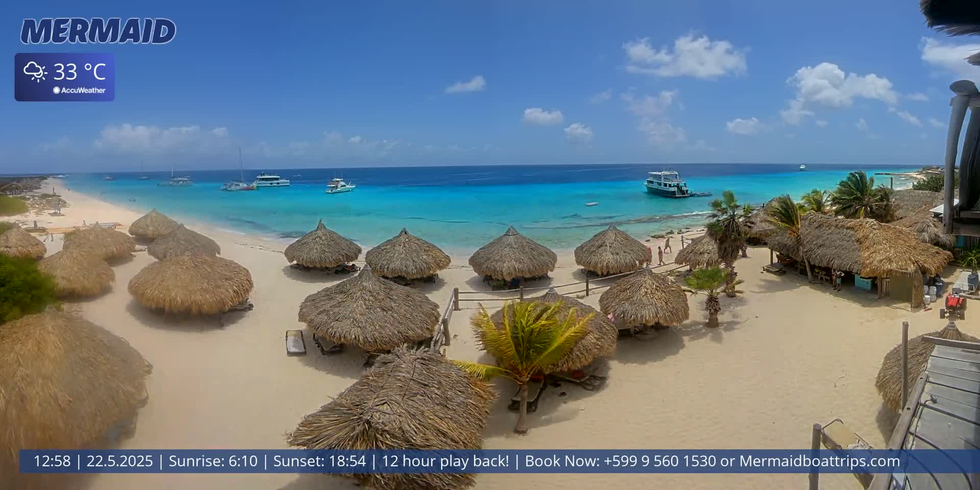 A sandy beach with thatched-roof huts, turquoise water, and several boats is visible under a mostly sunny sky; the temperature is 33°C.