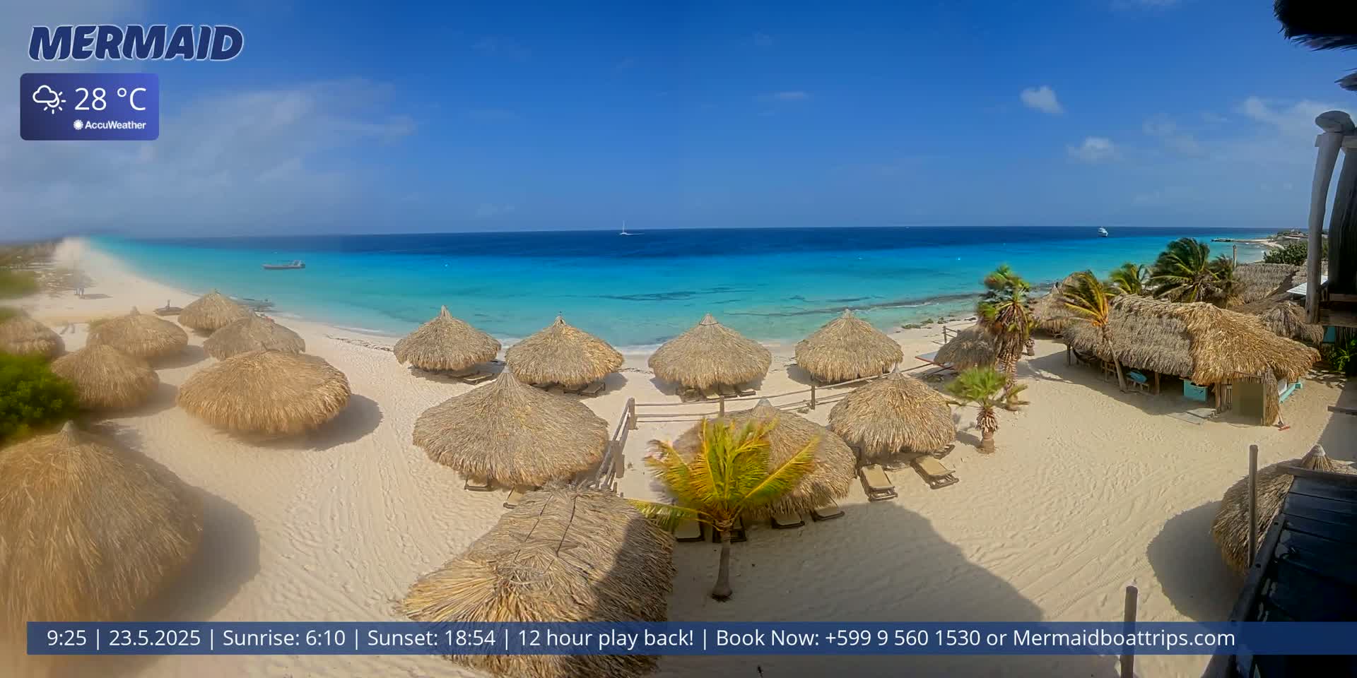 A sandy beach with numerous thatched-roof huts is situated next to a calm, turquoise ocean under a bright, sunny sky.