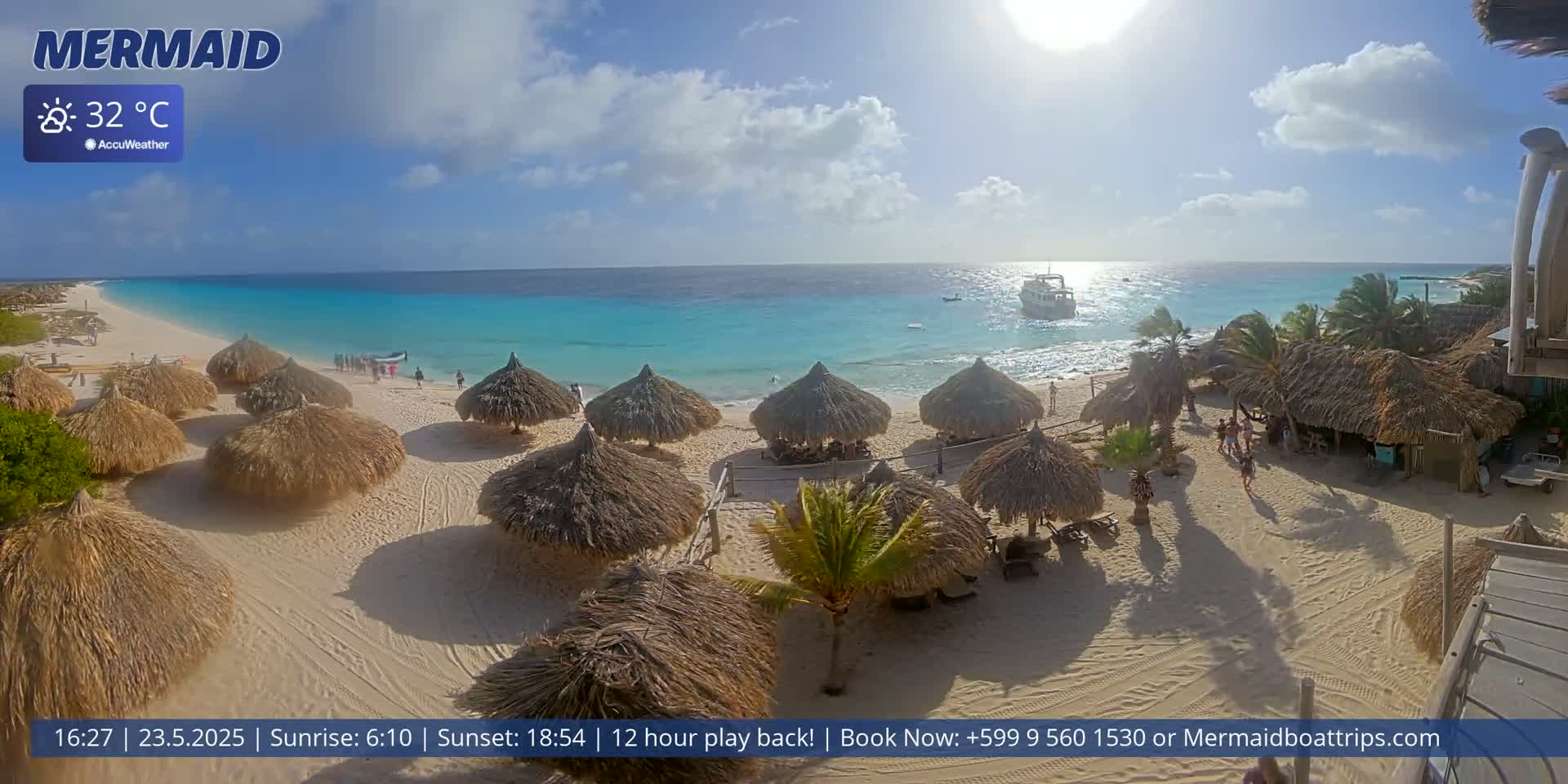 A beach with numerous thatched umbrellas, a few people, and a boat in the turquoise water under a sunny sky.