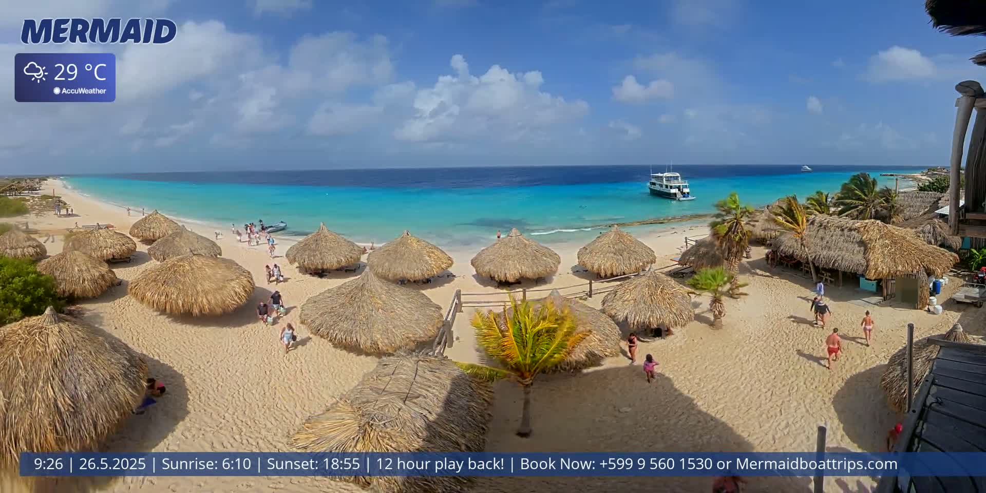 A beach scene with numerous thatched-roof umbrellas, a few people, and a boat on turquoise water under a partly cloudy sky.