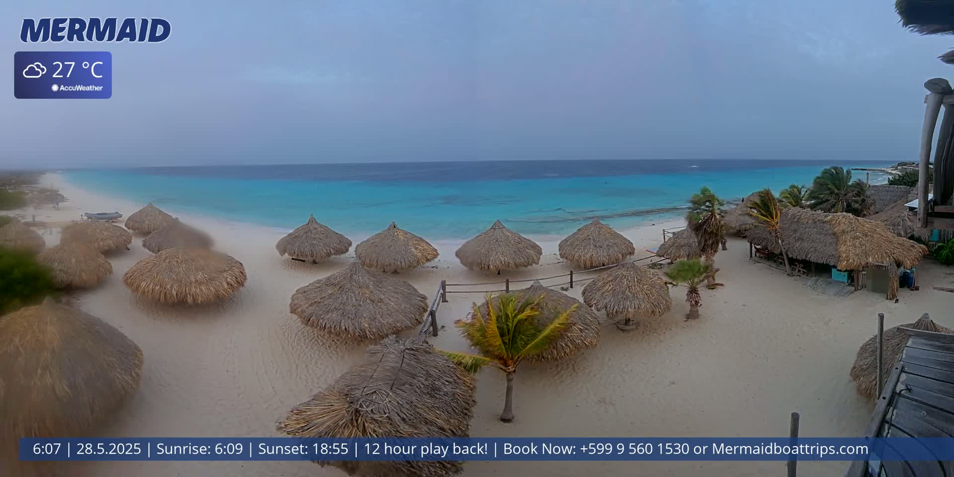 A beach with numerous thatched umbrellas and structures under an overcast sky, overlooking a calm turquoise ocean.