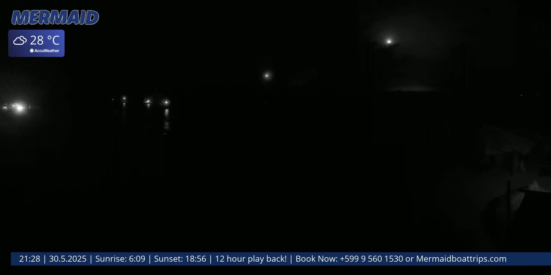 A nighttime, hazy scene shows a dark body of water with faint lights reflecting on its surface under a cloudy sky.