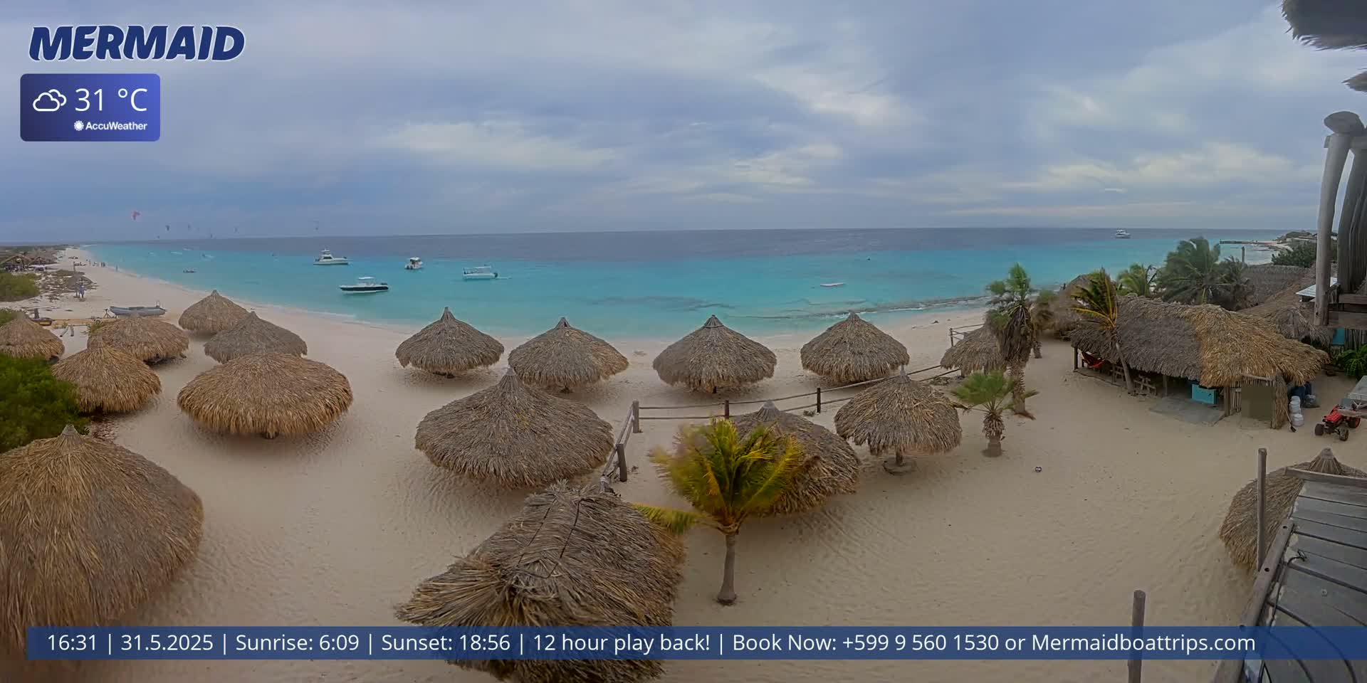 A sandy beach with numerous thatched-roof huts is shown, overlooking a calm turquoise ocean under a partly cloudy sky; the air temperature is 31°C.