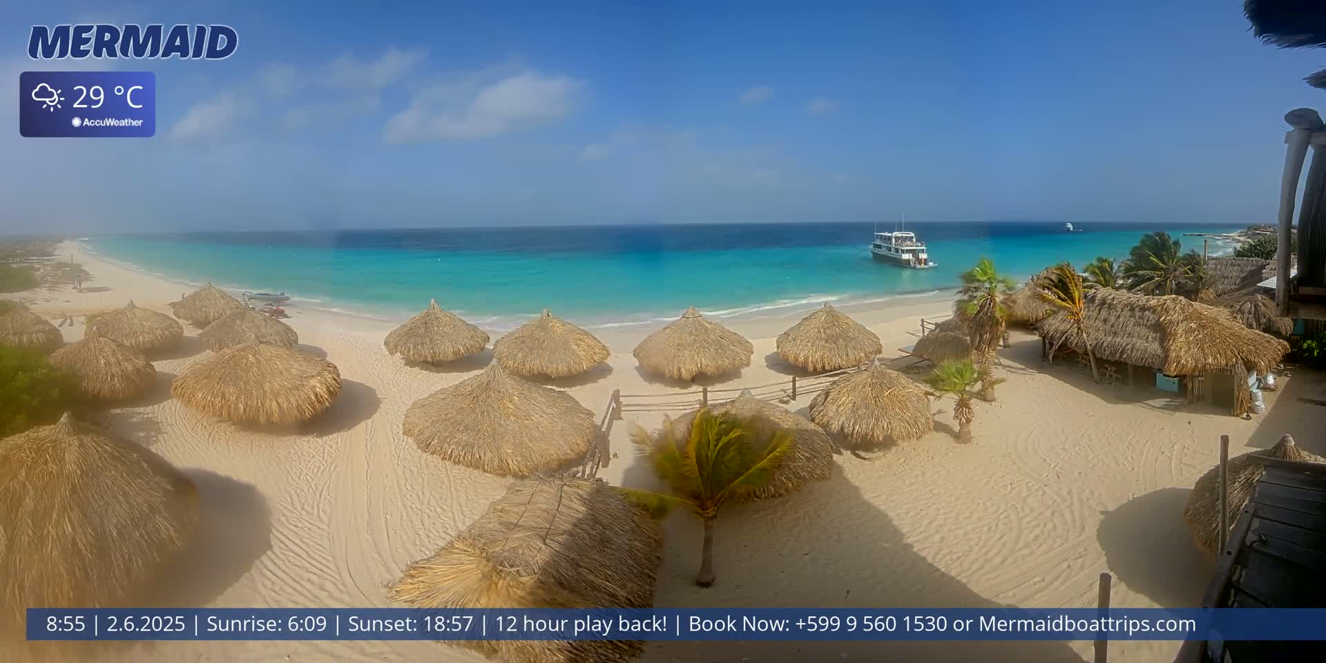 A sandy beach with numerous thatched-roof huts is shown, overlooking a calm, turquoise ocean under a clear, sunny sky; a boat is visible offshore.