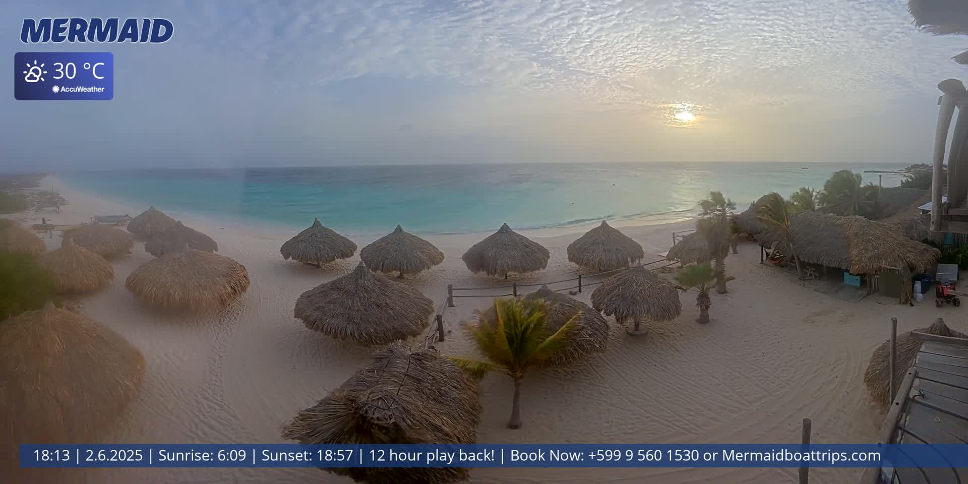 A hazy sunset over a beach with numerous thatched-roof umbrellas and a calm turquoise sea.