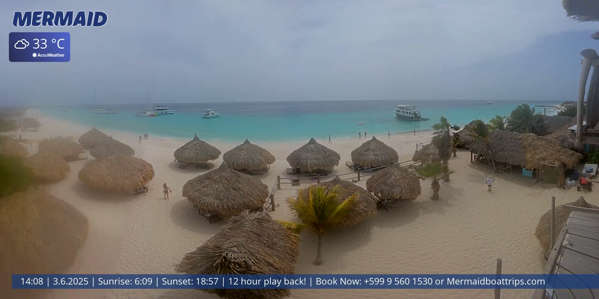 A hazy beach scene shows several thatched-roof huts on a sandy beach, with turquoise water and boats visible in the distance under a cloudy sky.