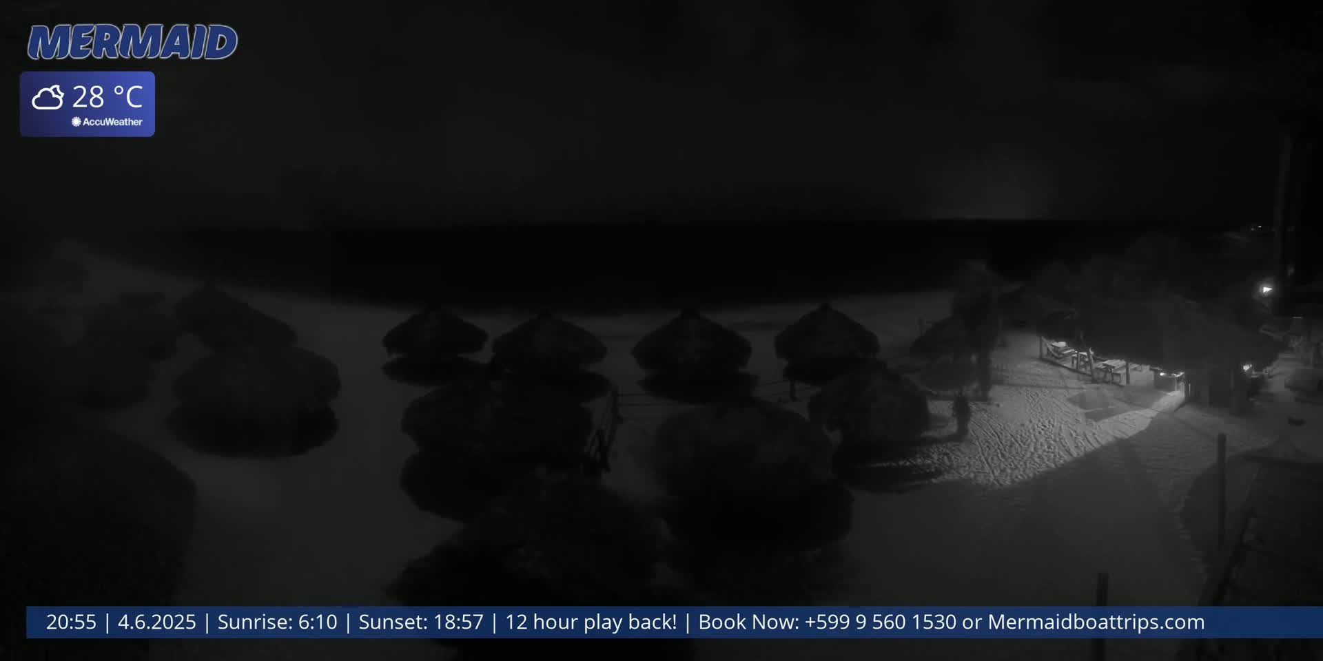 A nighttime beach scene shows several dark, umbrella-like structures on the sand near a dark building, under a clear, dark sky at 28°C.