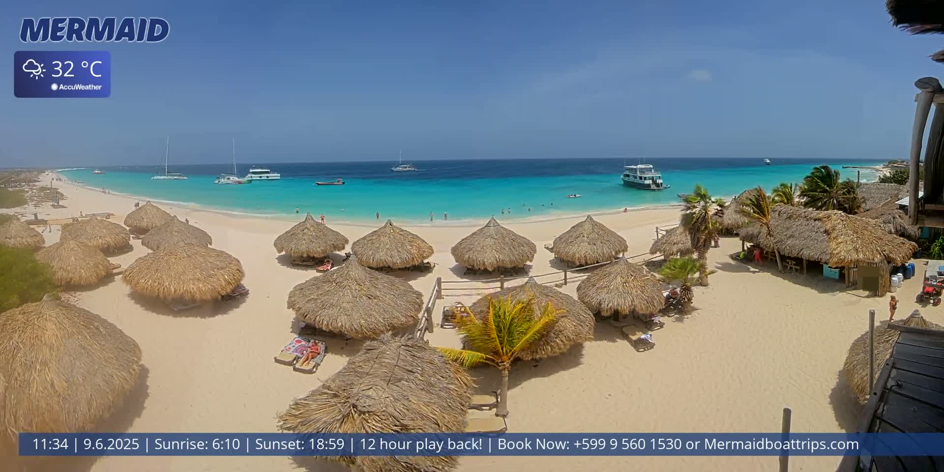 A sunny beach with turquoise water, numerous thatched-roof huts, and several boats in the distance.