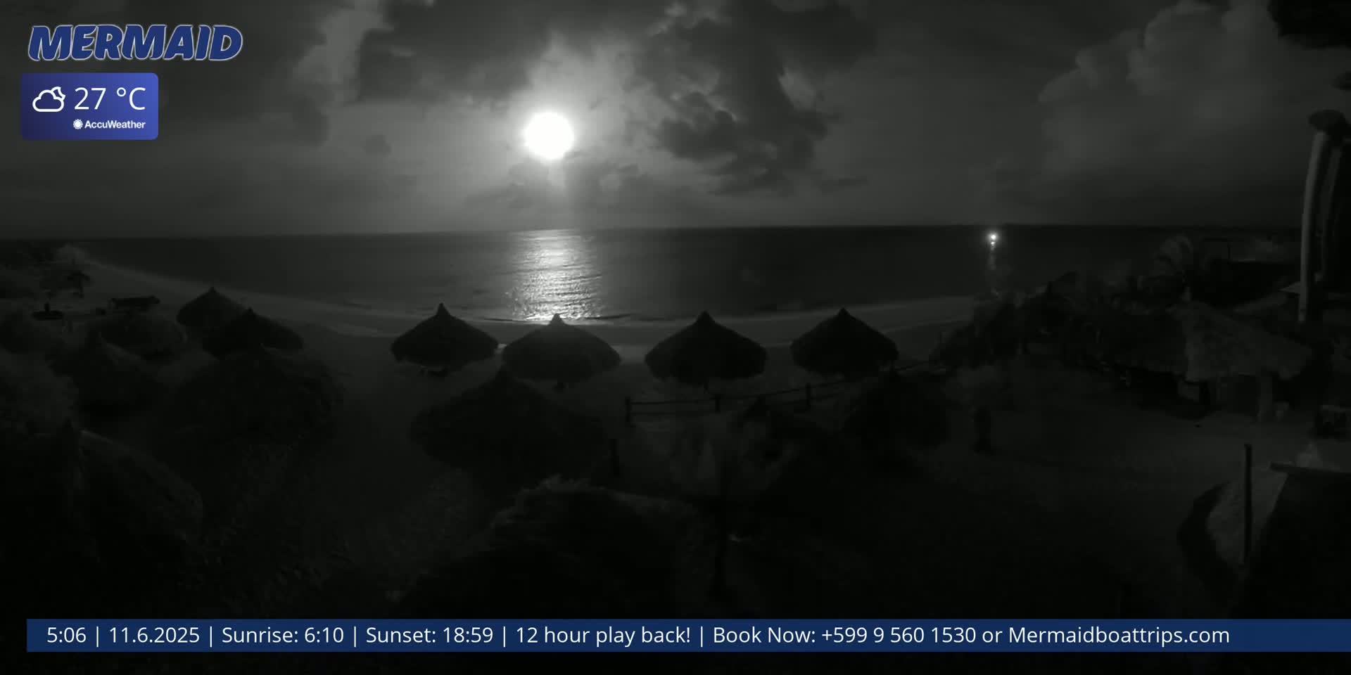 A nighttime beach scene shows a bright moon partially obscured by clouds over a calm ocean, with several thatched umbrellas on the sand.