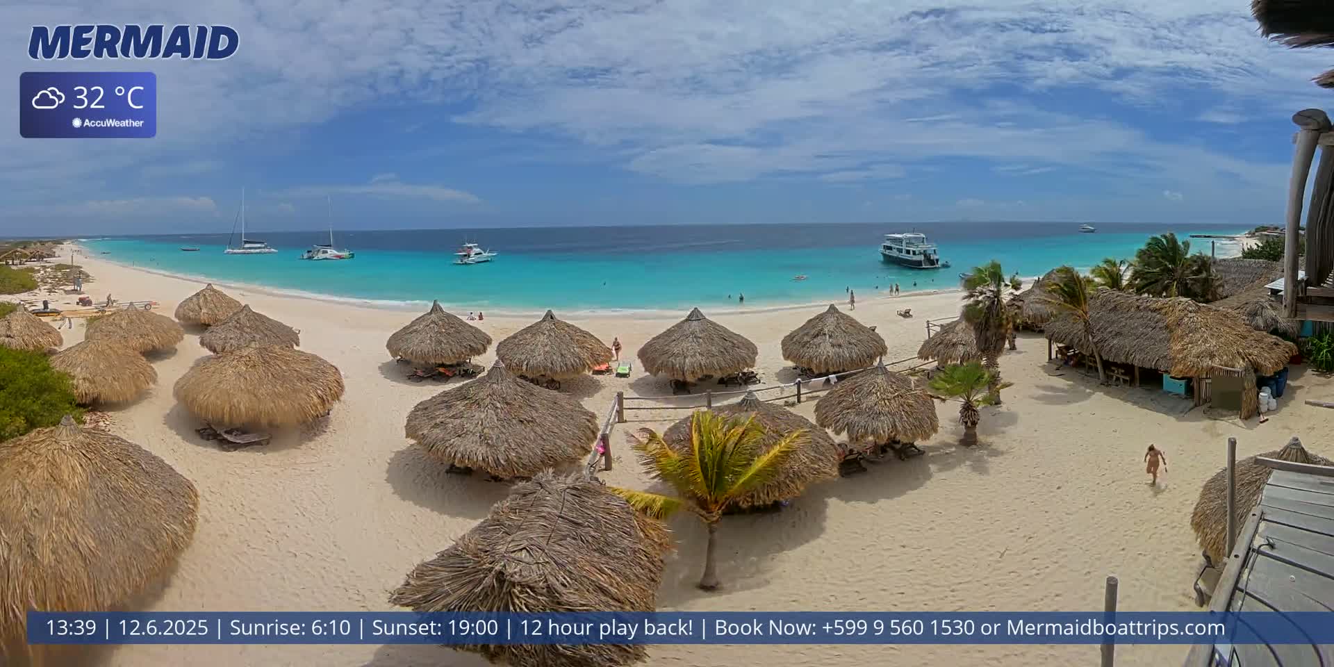 A beach with numerous thatched-roof huts, turquoise water, and several boats offshore under partly cloudy skies, with a temperature of 32 degrees Celsius.