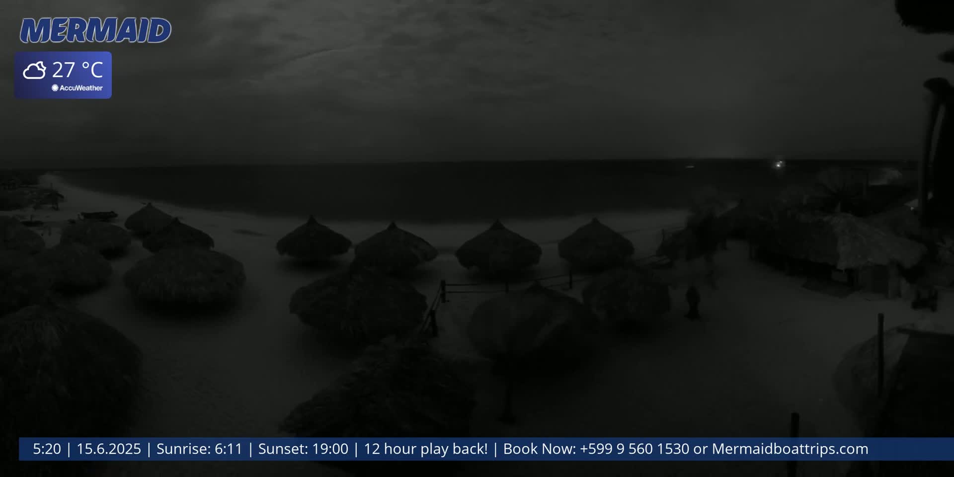 A nighttime beach scene shows several thatched-roof beach umbrellas on a sandy shore under a cloudy sky, with a calm ocean in the background.