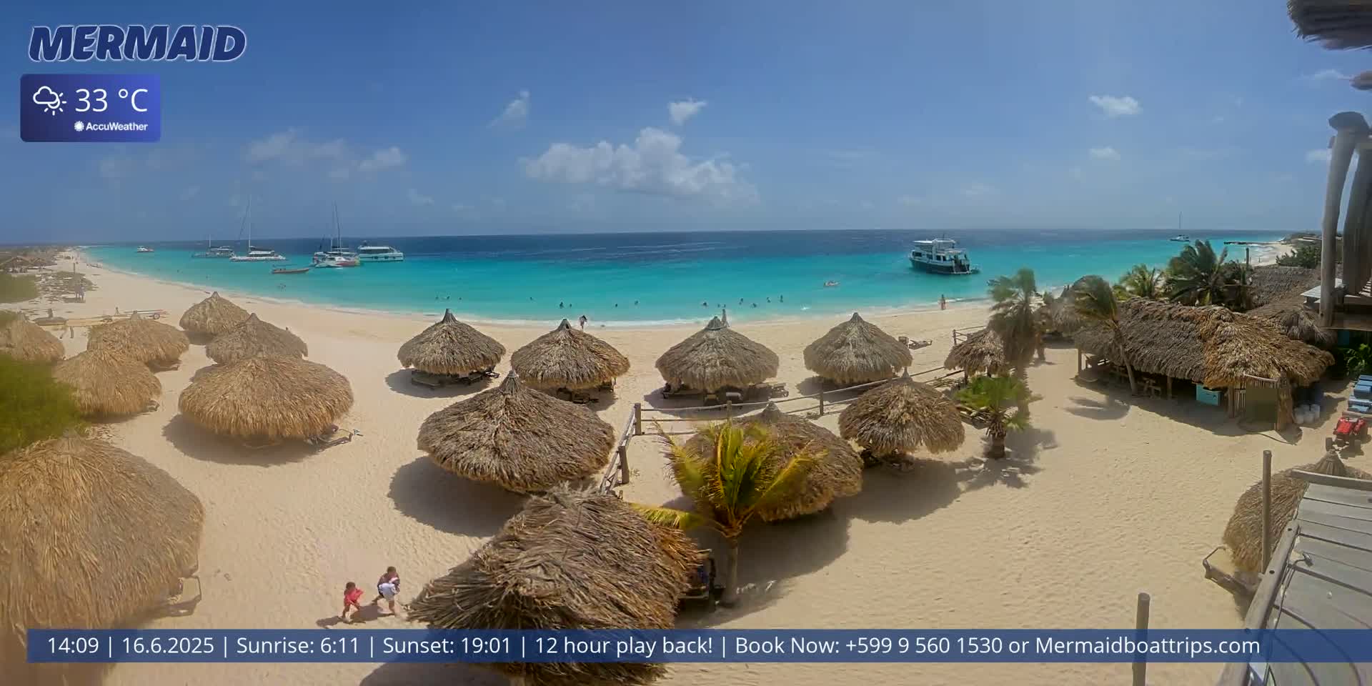 A beach with numerous thatched-roof huts, turquoise water, and several boats offshore under sunny skies.