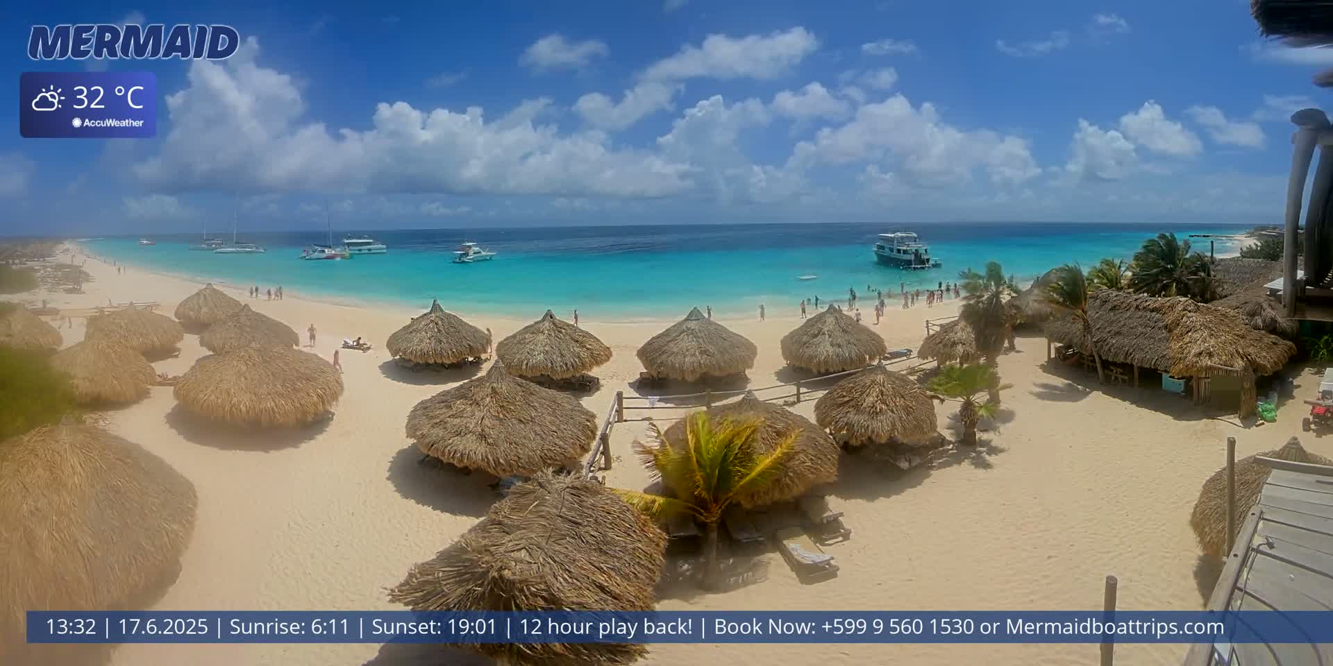 A sunny beach with turquoise water, numerous thatched-roof huts, and several boats offshore.