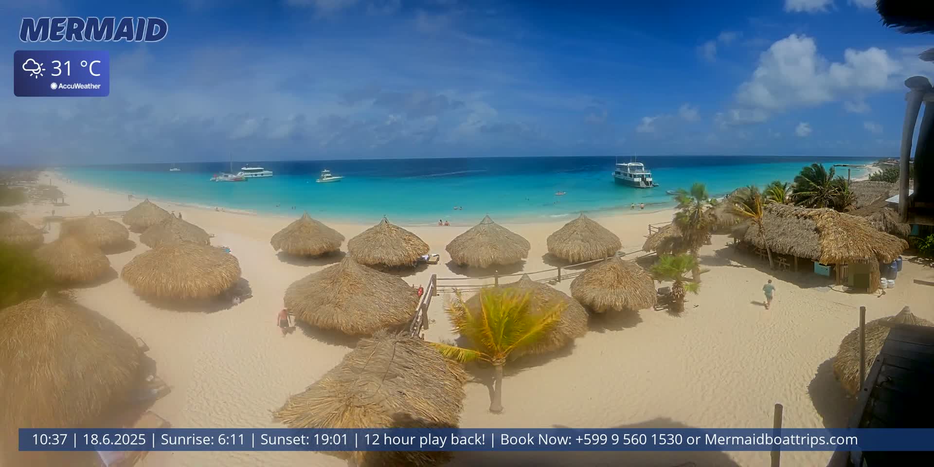 A sunny beach with turquoise water, several thatched-roof huts, and boats offshore, under a mostly clear sky with a temperature of 31°C.