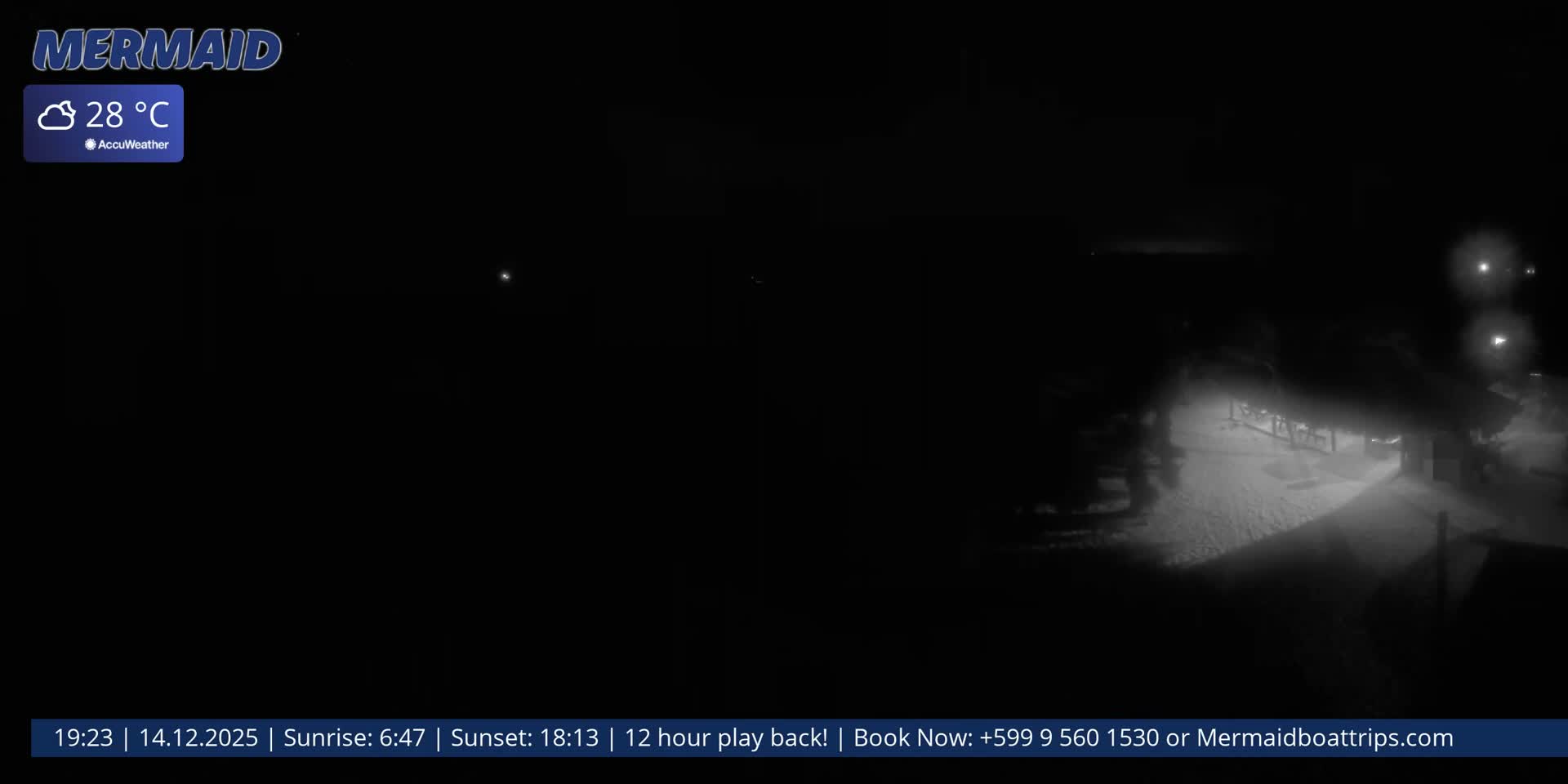 Under a cloudy night sky with a bright, obscured moon, a dimly lit beach features dark thatched umbrellas and a sailboat anchored in the calm ocean, reflecting distant lights.