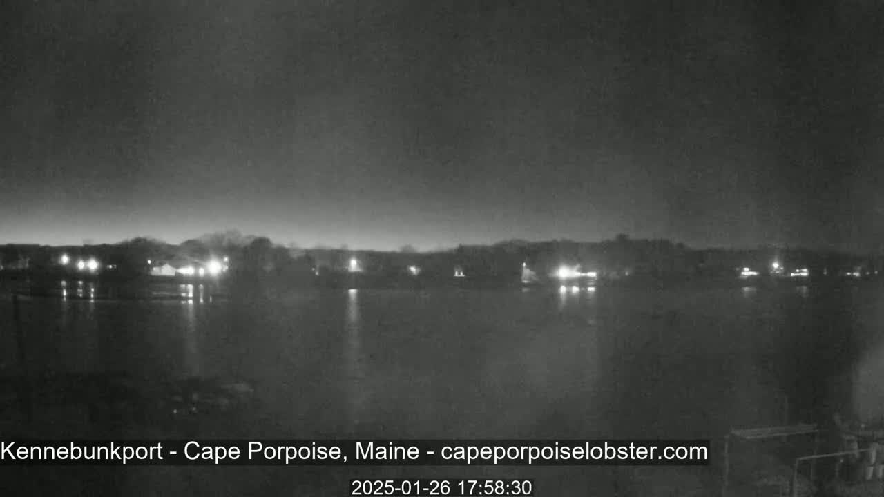 Here's a description of the image: A nighttime, low-light view of a calm body of water reflecting the lights of a distant shoreline under a clear, dark sky.