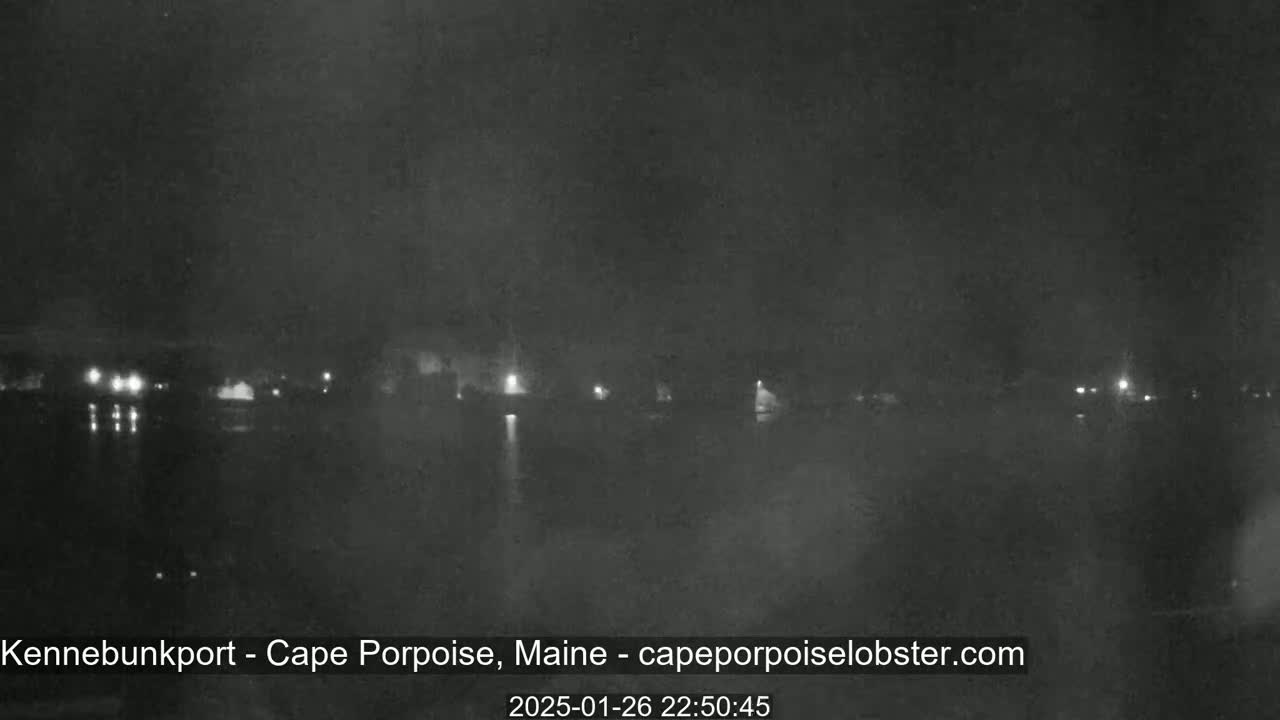 A nighttime, low-visibility view of a dark body of water with faintly visible lights on the opposite shore.