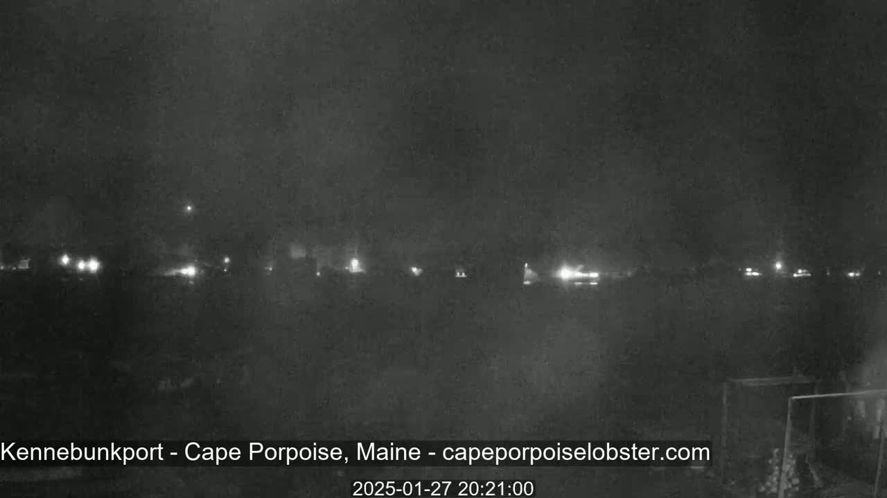 A nighttime, low-light view shows a line of faintly lit buildings or structures in the distance under a dark, possibly overcast sky.