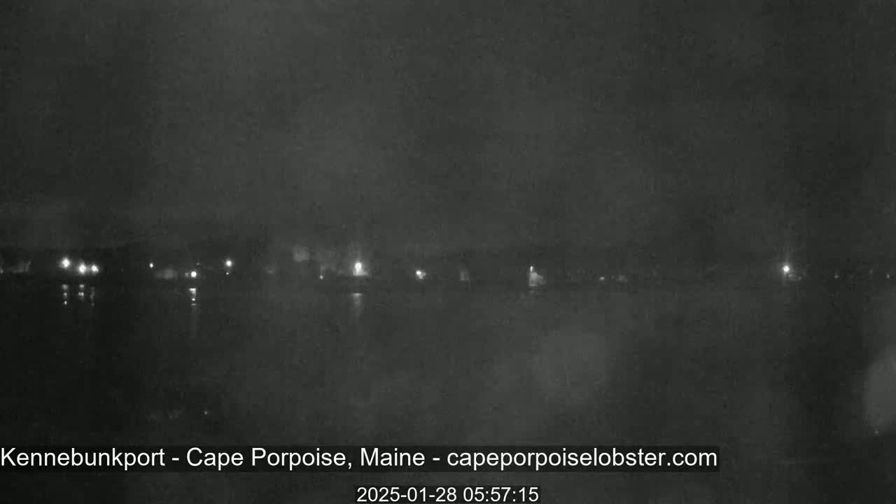 A nighttime, low-light view of a dark body of water with a dimly lit shoreline in the distance.