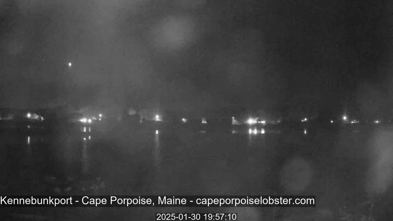 A nighttime view of a body of water with a town's lights faintly visible across it under a hazy sky.