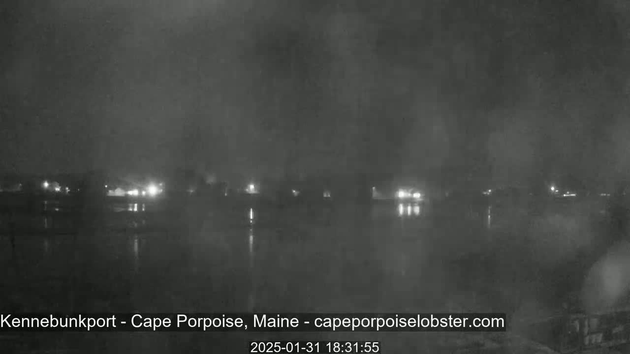 A nighttime, hazy view shows a body of water reflecting the faint lights of a distant town.