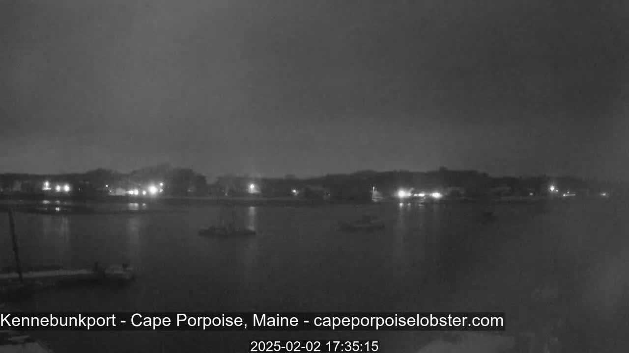 A nighttime, overcast view of a calm body of water with a shoreline of lights in the distance.