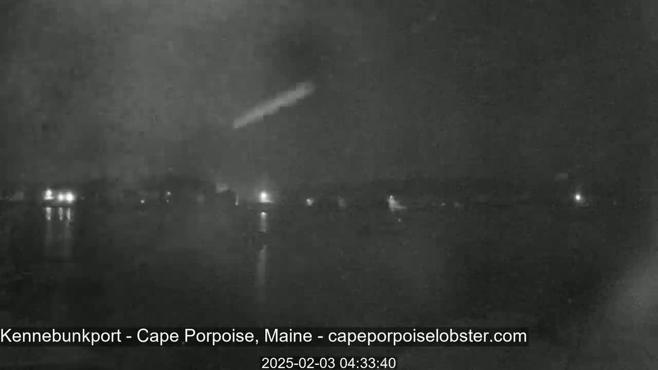 A nighttime, low-light view shows a body of water with a faint, blurry shoreline and a bright streak in the dark sky.