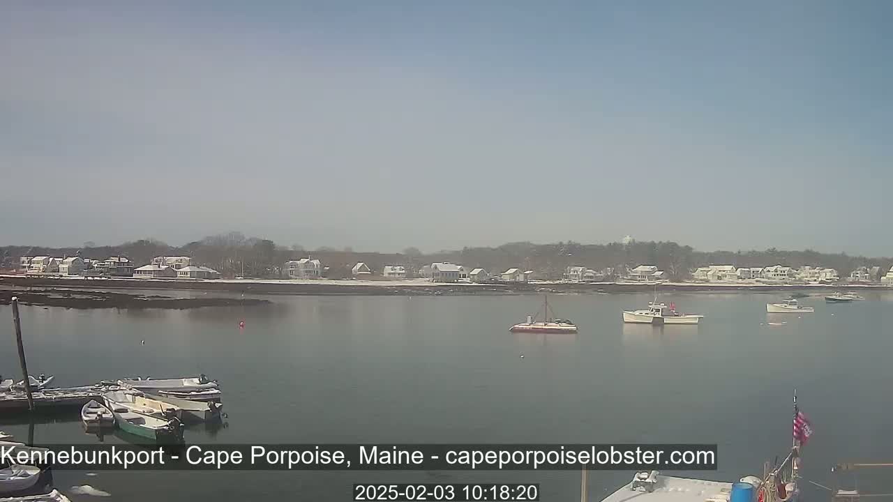 Several boats are moored in a calm harbor, with a snow-dusted shoreline of houses and trees visible in the background under a clear sky.