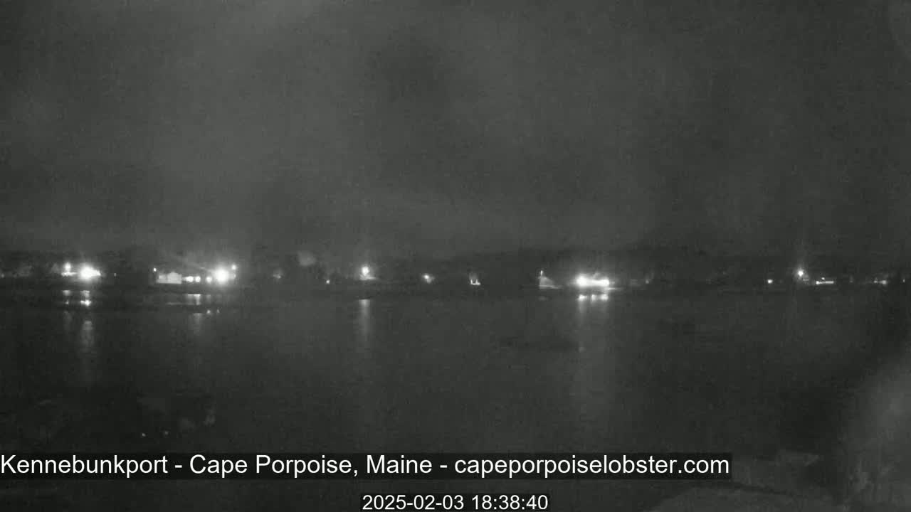 A nighttime, overcast view of a body of water reflecting the dim lights of a shoreline town.