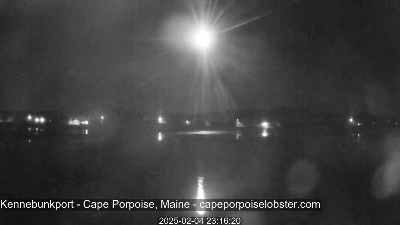 A bright light shines over a dark body of water at night, with a faint shoreline visible in the distance.