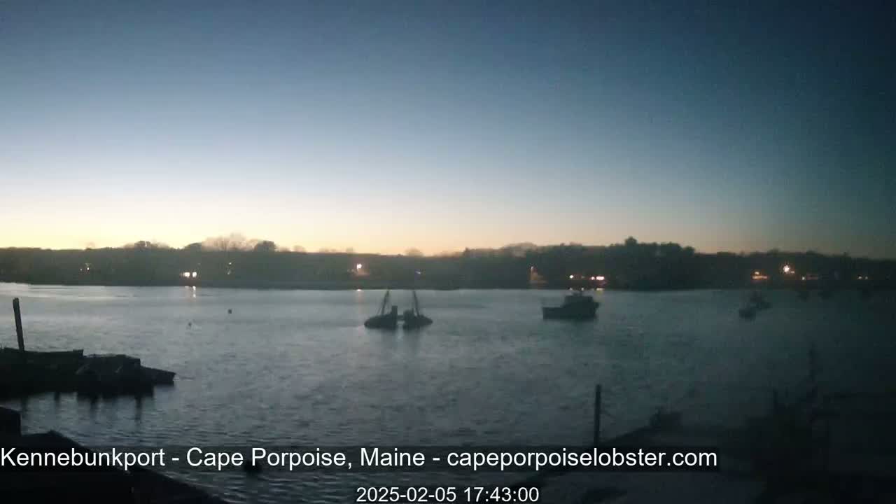 Several boats are moored on a calm body of water at dusk, with a landmass visible in the background.