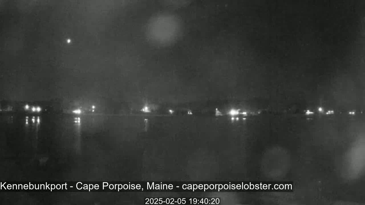 A nighttime, slightly hazy view of a calm body of water reflecting the lights of a distant shoreline.
