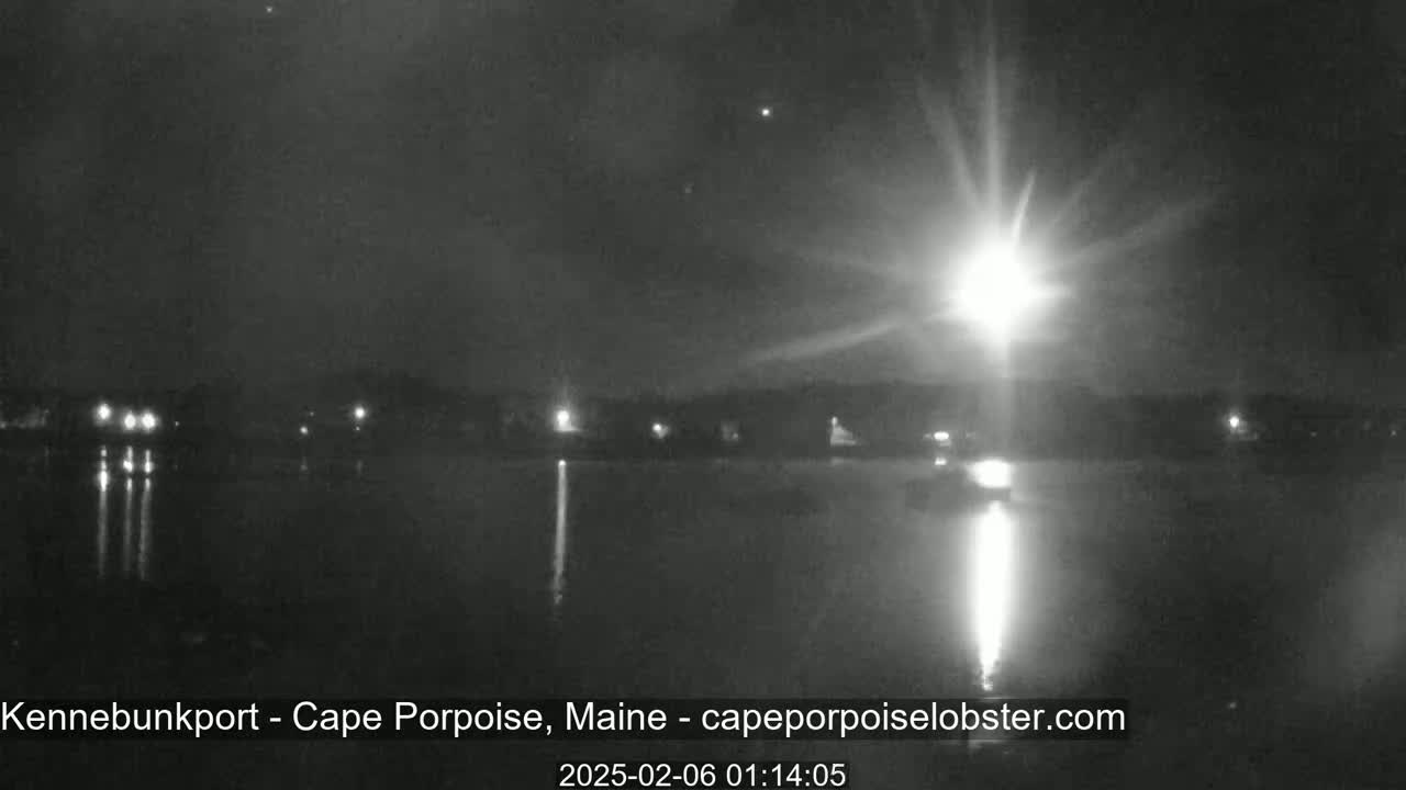 A bright light shines over a dark body of water at night, with a dark shoreline visible in the distance.