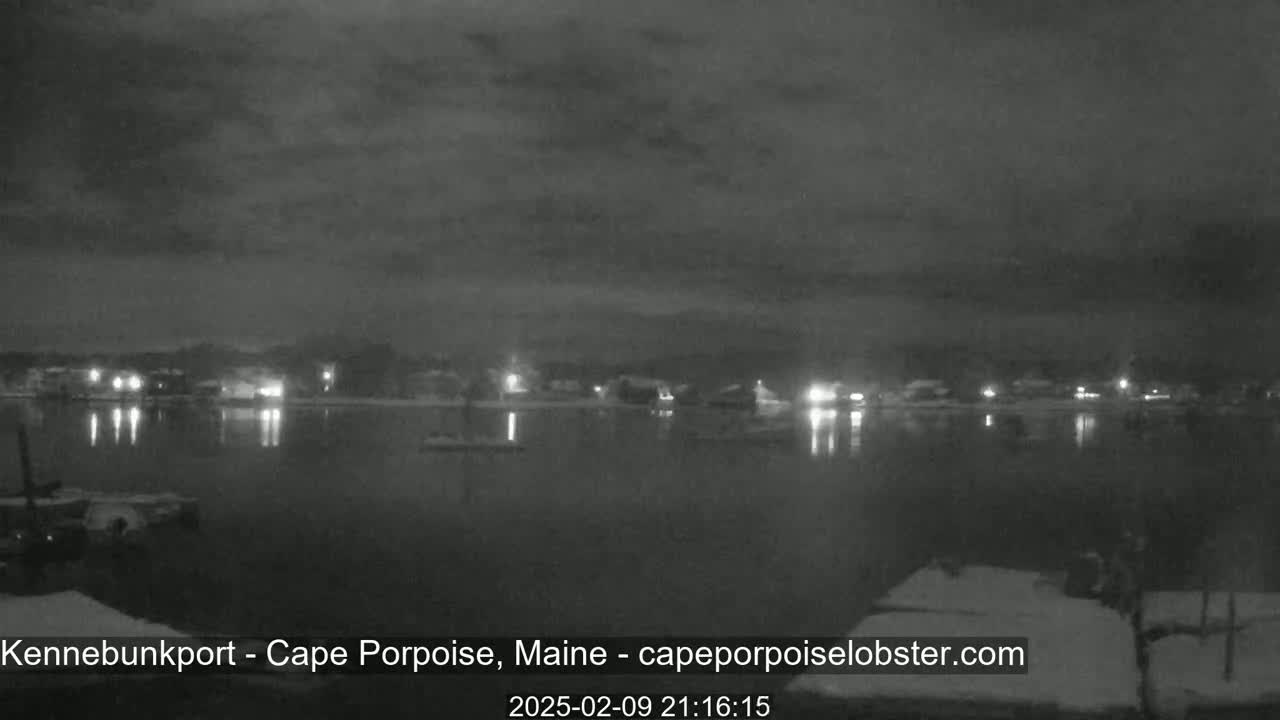 A nighttime view of a calm body of water reflecting the lights of a town under a cloudy sky.