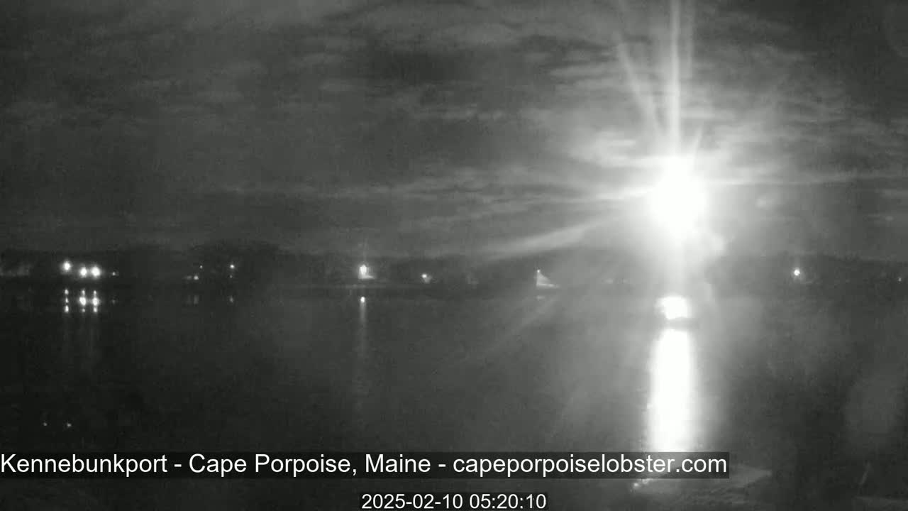 A nighttime view of a body of water with a bright light source in the distance under a cloudy sky.