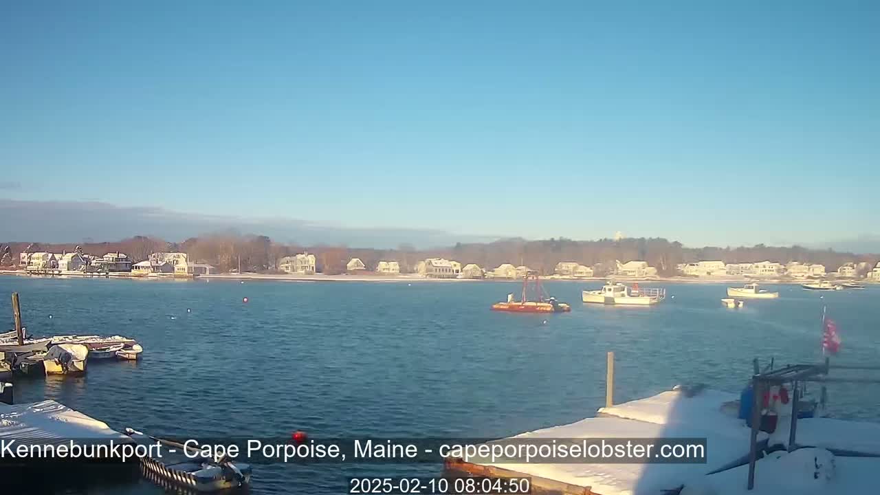 A calm body of water with several boats and a snow-covered shoreline under a clear blue sky.