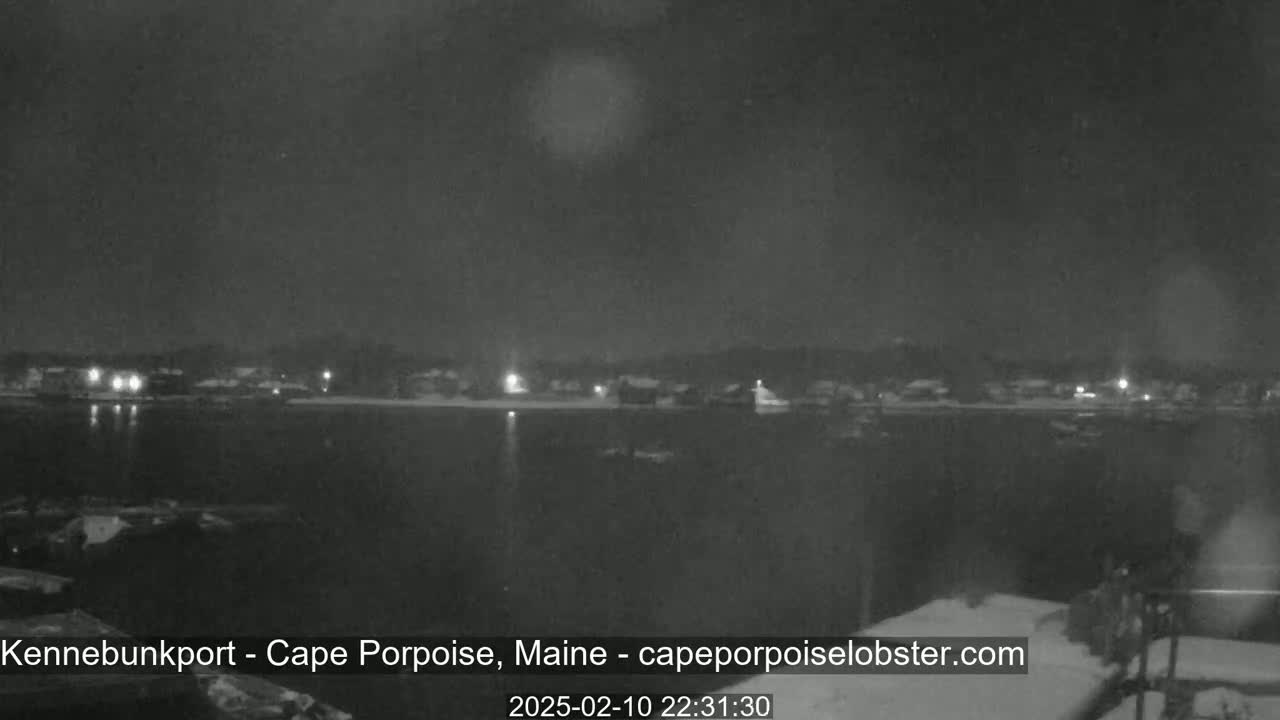 A nighttime view of a calm body of water with a snow-covered shoreline and dimly lit buildings across the water.