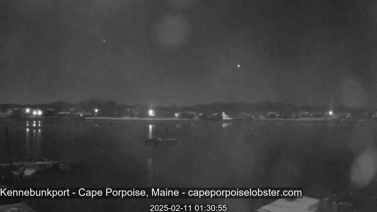 A nighttime, low-light view of a calm body of water with a shoreline of dimly lit buildings under a slightly cloudy sky.