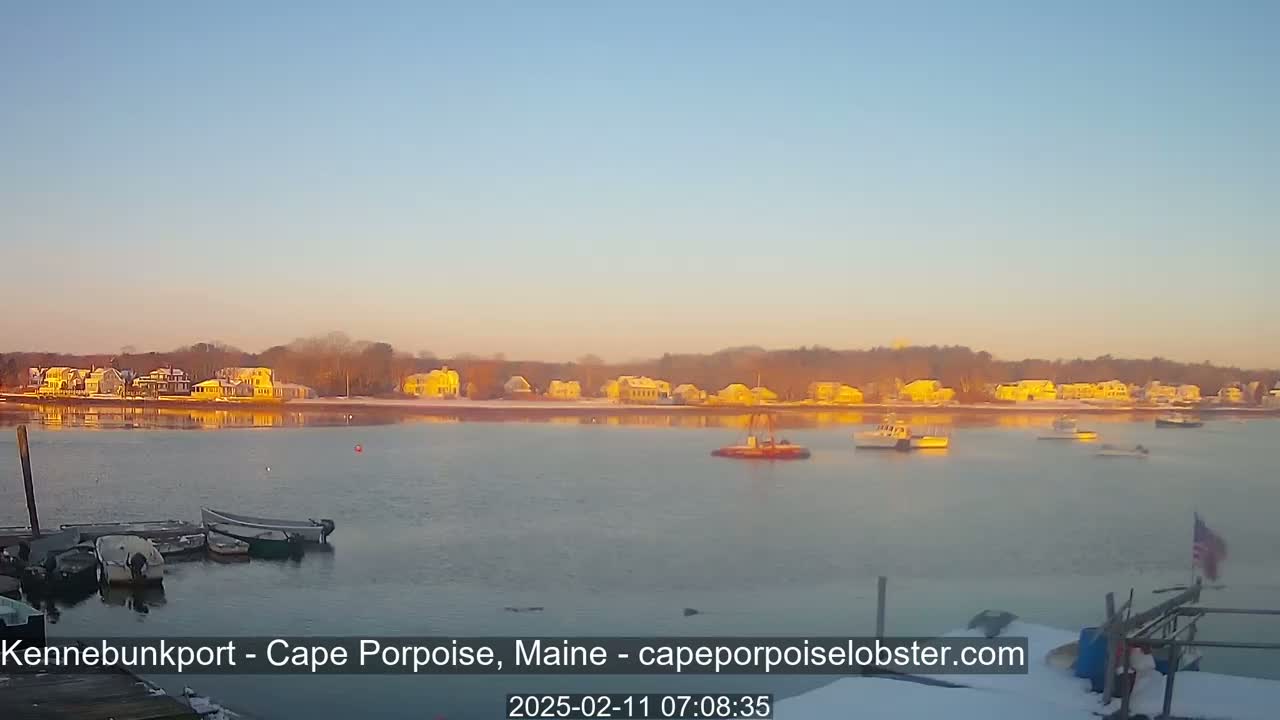 A calm body of water reflects the golden light of sunrise illuminating a shoreline of houses covered in snow.