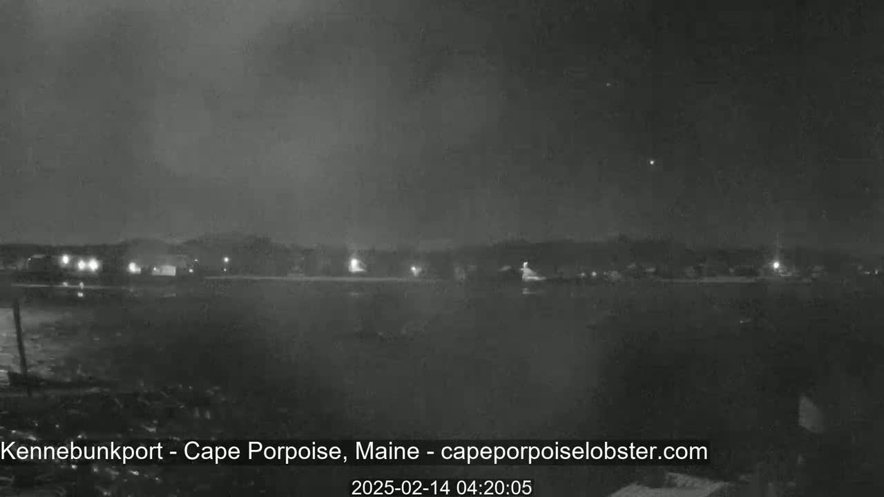 A nighttime, low-light view of a dark, flat landscape with a few distant lights and a dark sky.