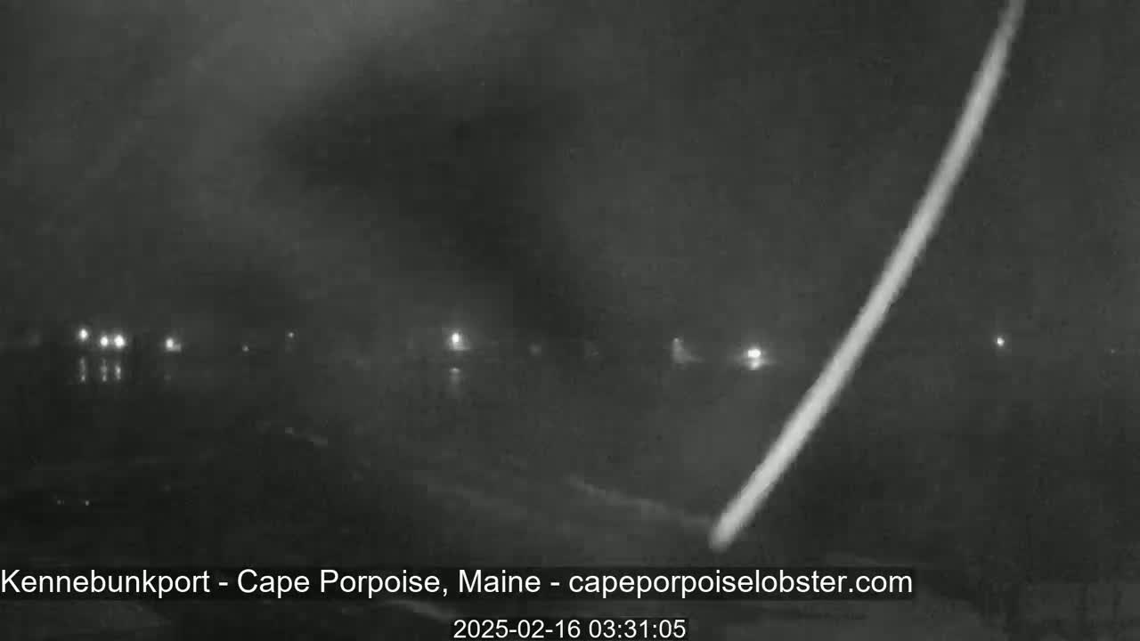 A bright streak of light diagonally crosses a dark, hazy, nighttime scene of a road with distant lights.