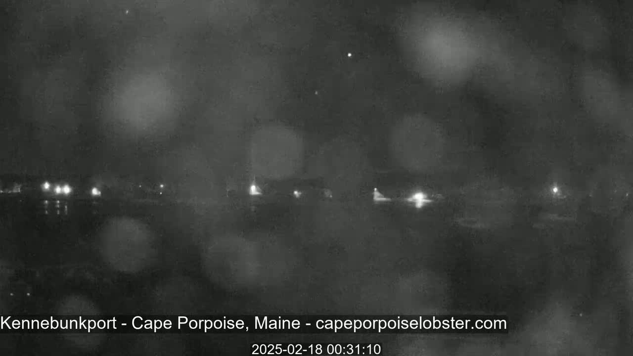 A nighttime, blurry, low-light view of a waterfront area with faint lights and what appears to be light rain or mist.
