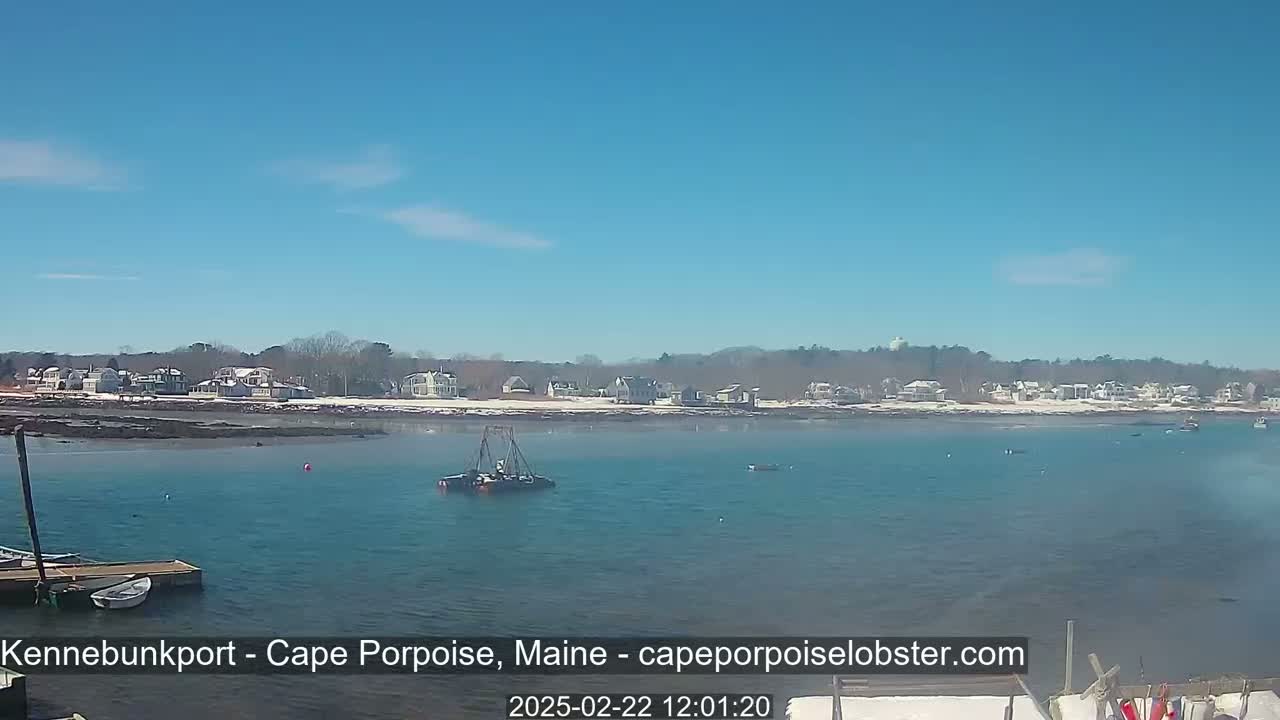 A calm body of water with a few boats and a shoreline of snow-covered houses under a clear blue sky.