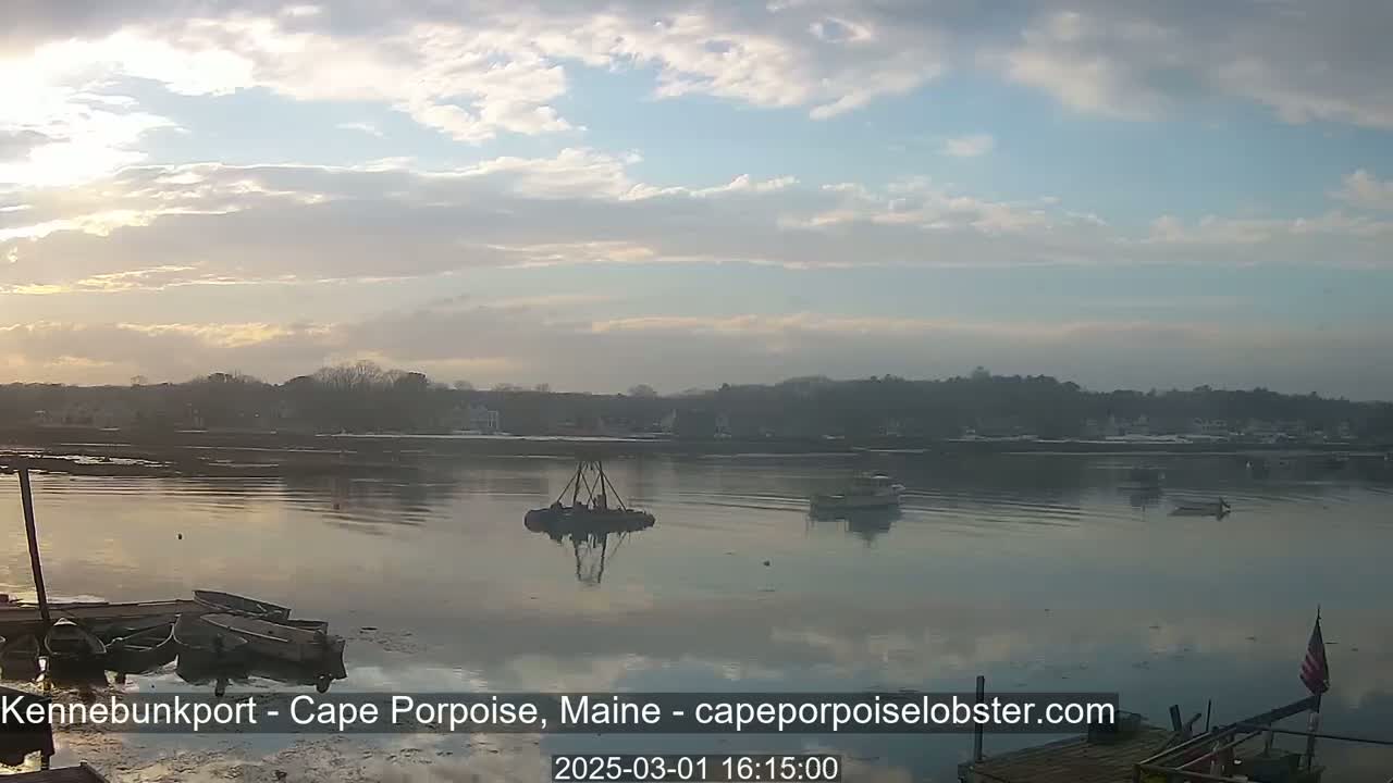 A calm body of water with several small boats and a larger piece of equipment is visible, under a partly cloudy sky.