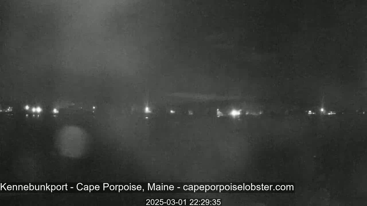 A nighttime, low-light view of a dark body of water with a distant shoreline showing faint lights.