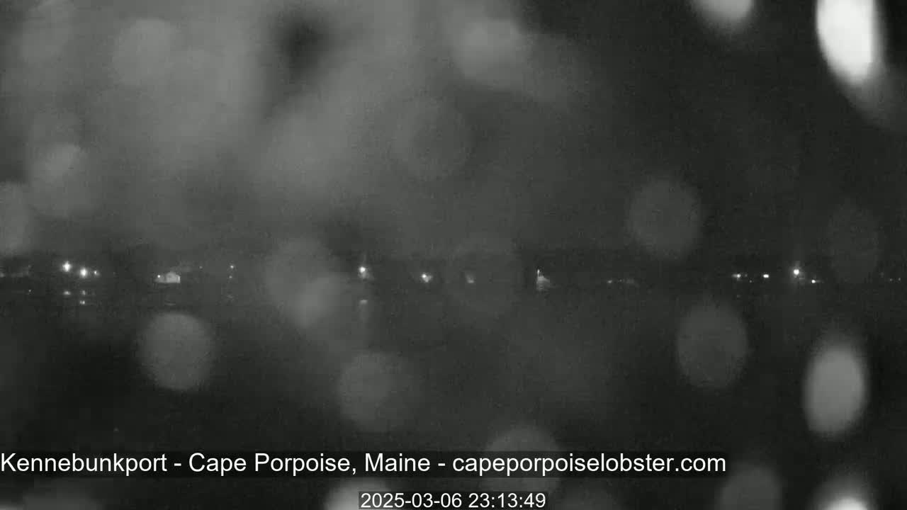 A nighttime, blurry view of a town or cityscape under rainy conditions, with faint lights visible in the distance.