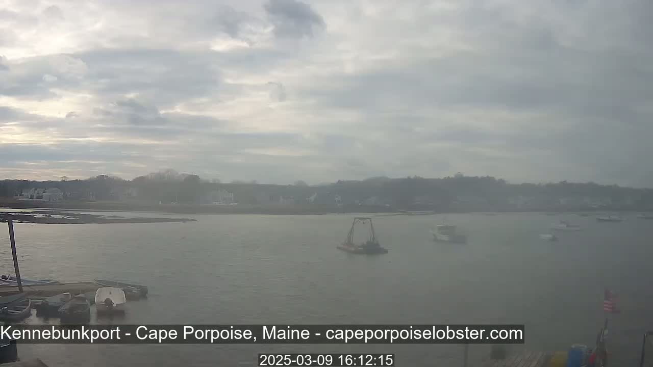 A hazy, overcast day reveals a calm body of water with several boats, including a small lobster boat, and a shoreline with buildings in the distance.