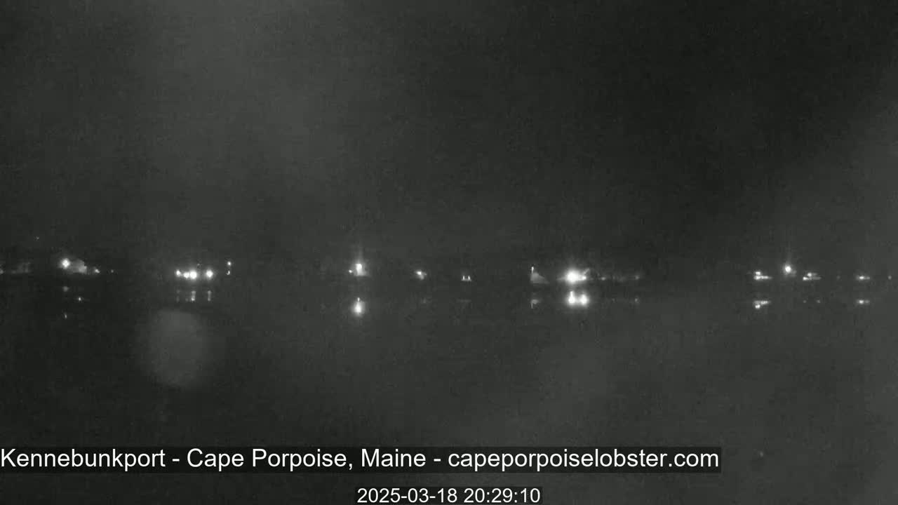 A nighttime, low-light view shows a dark body of water with a line of distant lights across it.