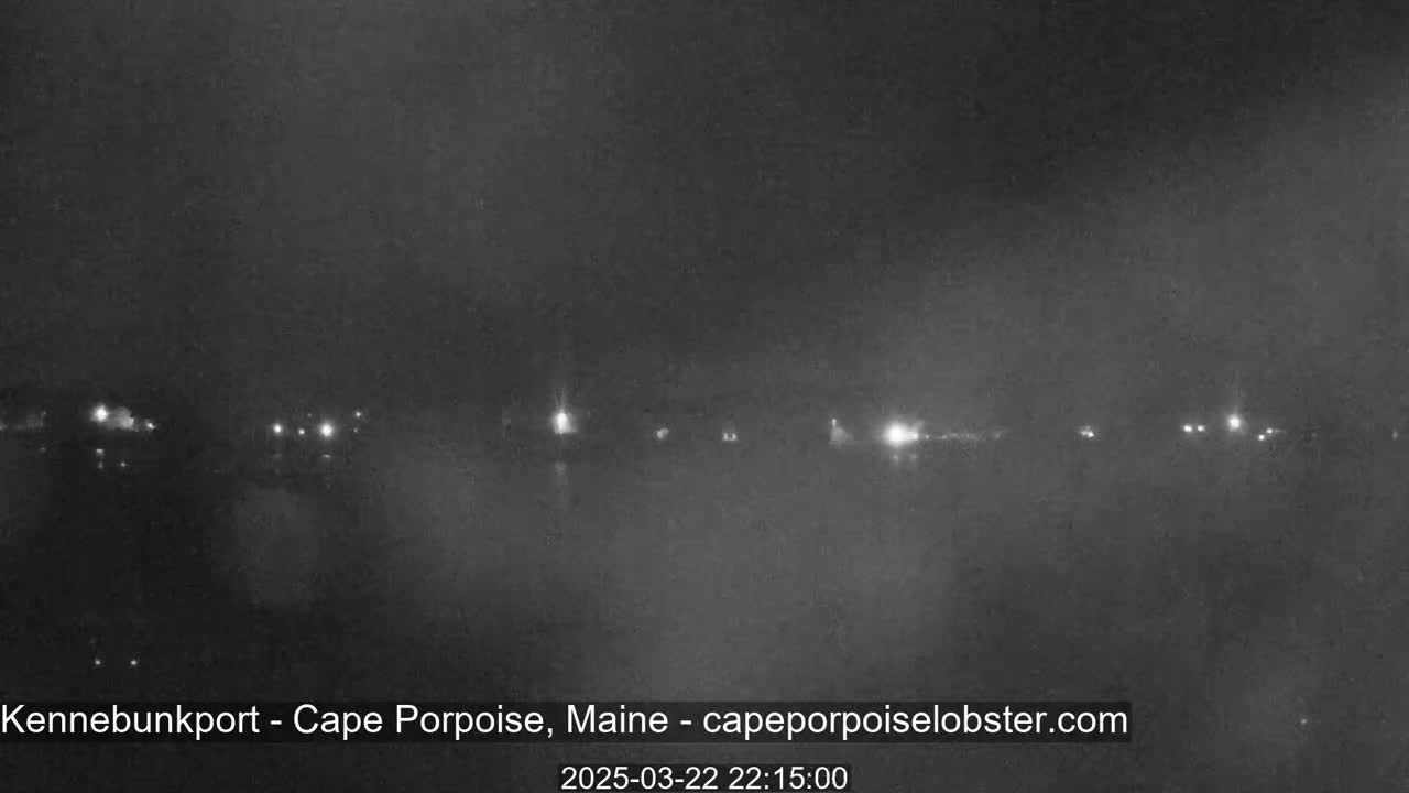 A nighttime, hazy view of a shoreline with scattered lights visible in the distance.