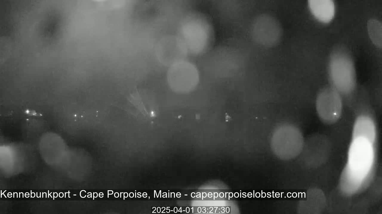 A blurry, nighttime image shows indistinct lights in the distance through heavy fog or rain.